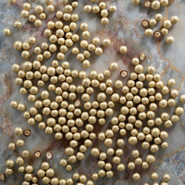 A close-up image of small, round, gold-coated hazelnuts on a marbled background.