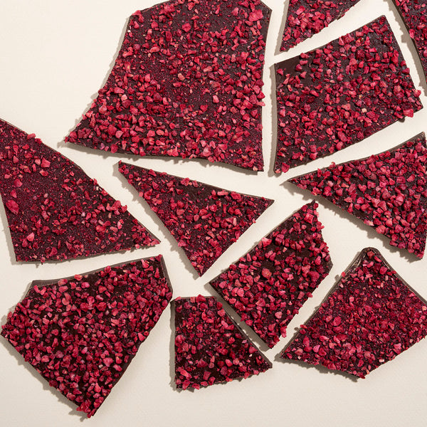 Handmade dark chocolate bark with visible freeze-dried raspberry pieces scattered on a white surface.