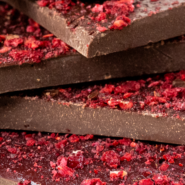 Stacked pieces of dark chocolate bark with freeze-dried raspberry pieces scattered around.