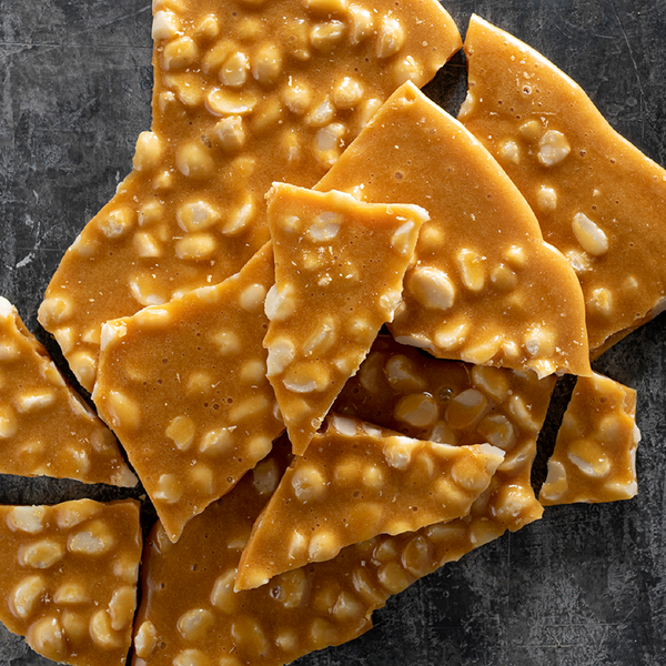 Shards of Australian Made macadamia brittle with visible nuts on a dark surface