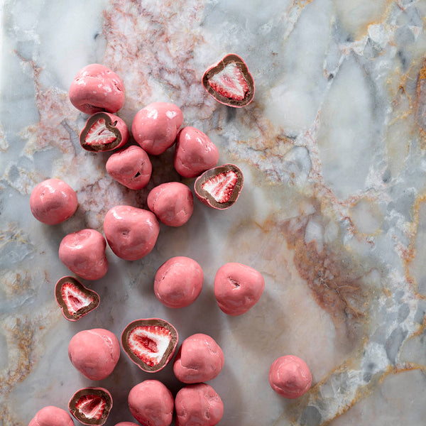 A collection of milk chocolate coated whole freeze-dried strawberries arranged on a marble surface.