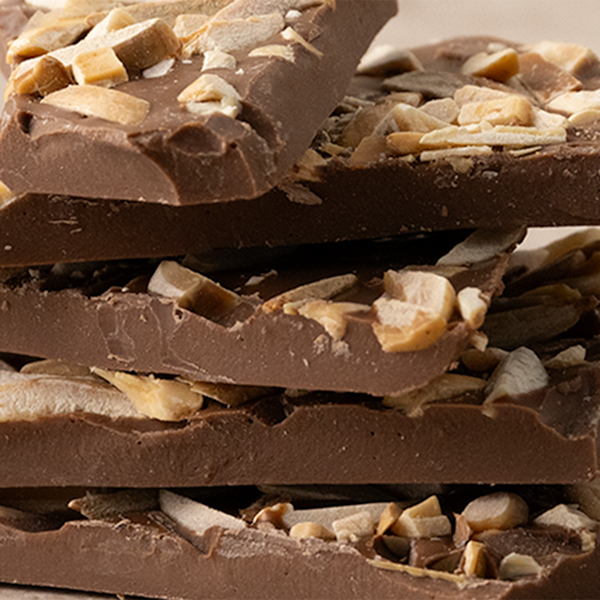 Stacked pieces of milk chocolate bark with smoked salt and roasted almonds on a light background.