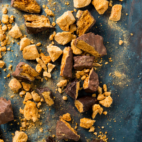 Chunks of milk chocolate with honeycomb pieces scattered on a surface.