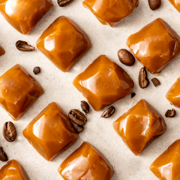 Multiple square espresso caramels arranged on a surface with coffee beans scattered around.