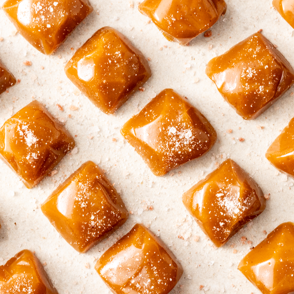 A close-up image of multiple salted caramels with a glossy finish, sprinkled with sea salt on a white surface.