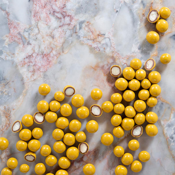 Chocolate-coated macadamia nuts with a passionfruit coating, displayed on a marble surface.