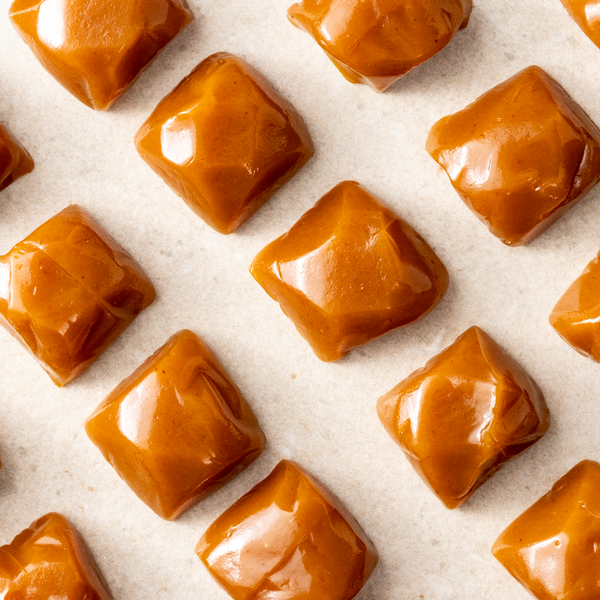 A collection of square caramel candies with a glossy finish, arranged in a pattern on a light-colored surface.